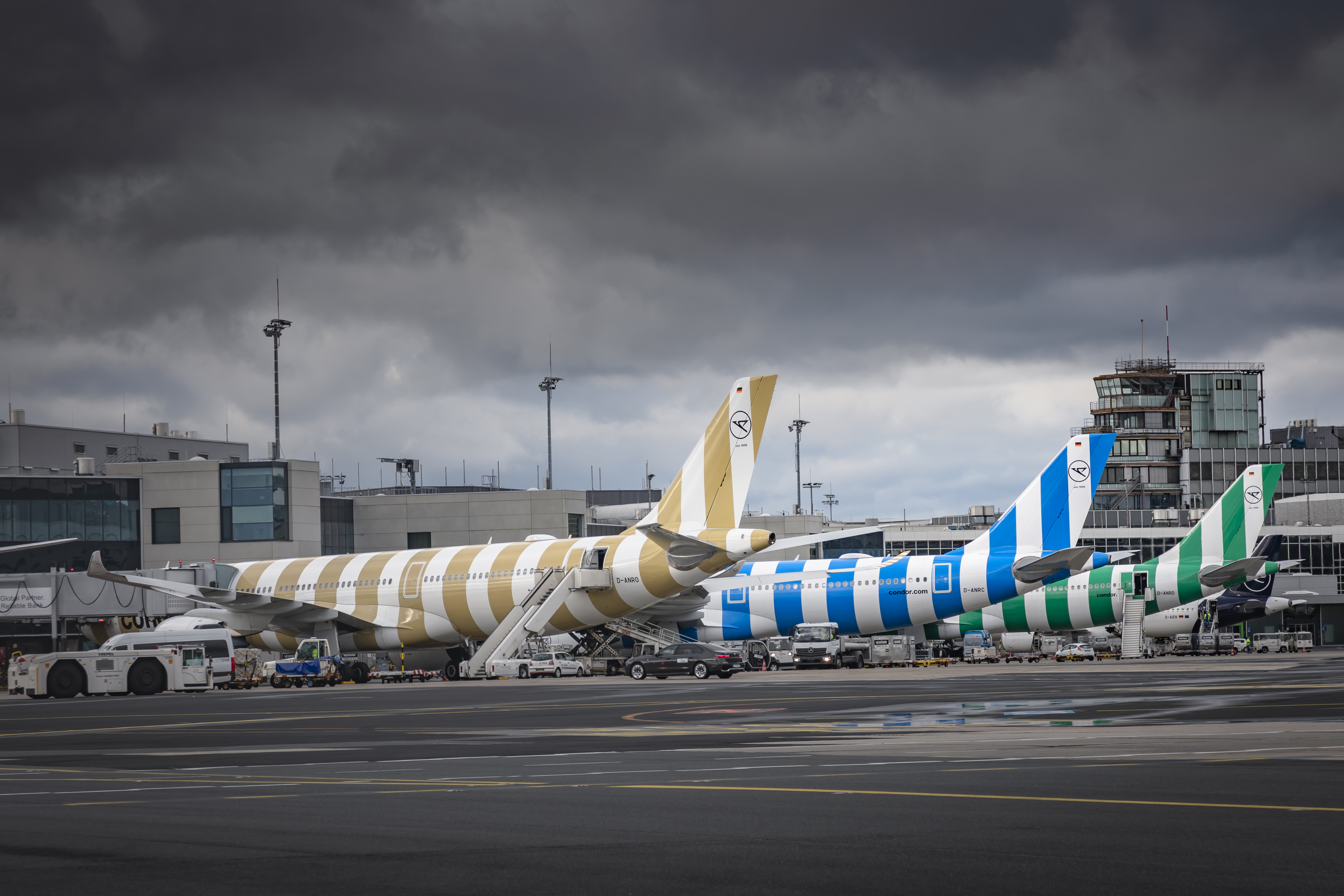 Condor aircraft with striped livery on the airport apron beneath a cloudy sky.