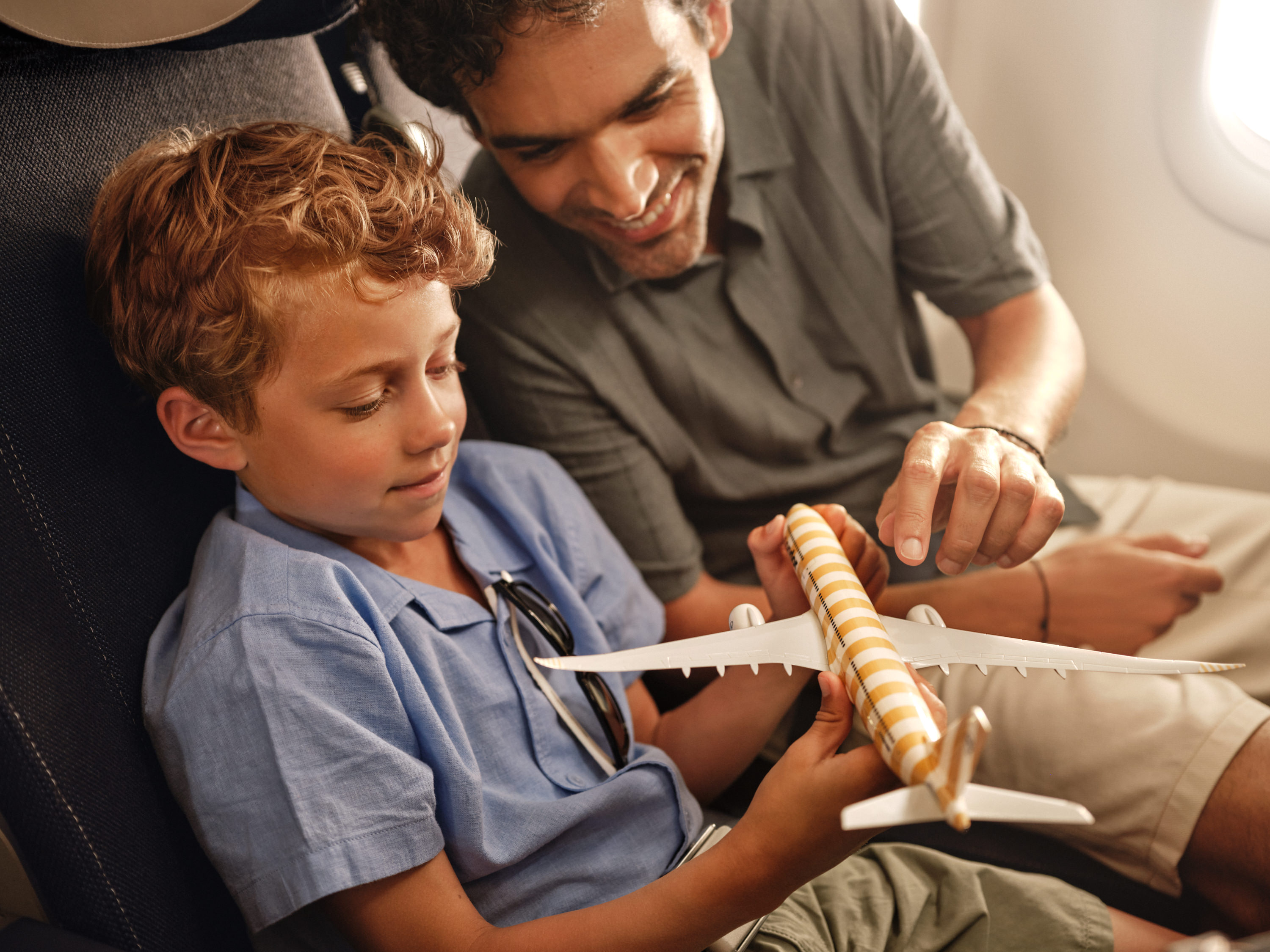 A child and an adult are sitting in an aircraft seat, looking at a model plane.
