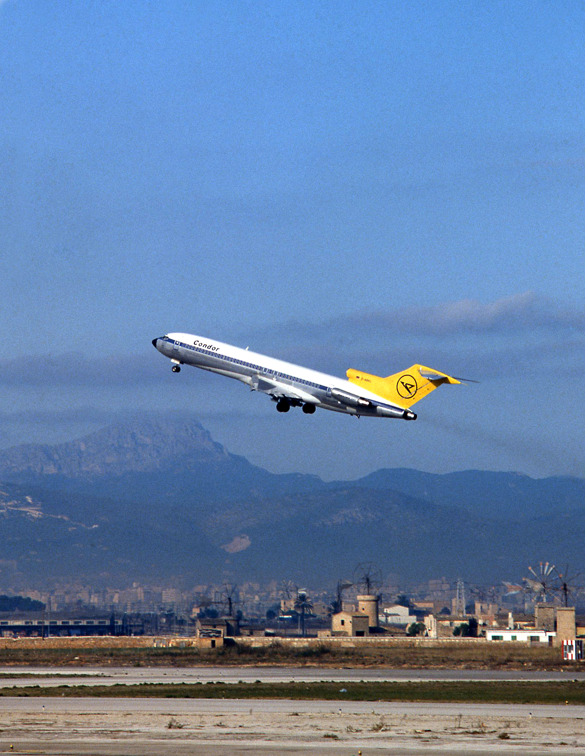 Historic passenger aircraft with a yellow tail unit flying over a mountainous landscape.